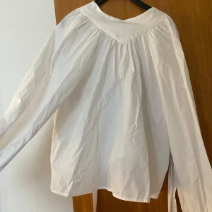 Vit långärmad henley i bomull - Säljer en denna vita blusen, den är halvpolo som man knyter i nacken. Den har puffiga ärmar med vilket ger en fin detalj! Den är endast testad av mig men jag har själv köpt den second hand, däremot är den i väldigt fint skick.