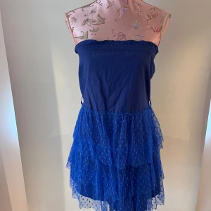 Blå axelbandslös klänning Ida Sjöstedt - Supersöt blå axelbandslös kortklänning från Ida Sjöstedt med volangkjol i flera lager av prickig tyll. Klänningen har hållare för bälte också (bältet på bilden ingår inte) Köptes secondhand. 