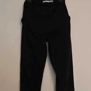 Svarta kostymbyxor i rak modell - Snygga svarta kostymbyxor med klassisk rak passform. Finns bälteshällor och fickor.