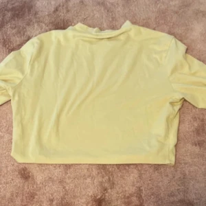 Gul croppad tröja från Monki - Snygg gul croppad tröja från Monki i mjuk bomull. Tröjan har en avslappnad passform med trekvartsärm och rund halsringning. Perfekt för dig som gillar en chill och färgglad stil.