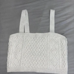 Ljusgrå stickad linnetopp från H&M - Superfin ljusgrå stickad linnetopp från H&M med breda axelband och snyggt flätmönster framtill. Toppen har ribbade kanter och en mjuk, mysig känsla som passar perfekt till jeans eller kjol. Enkel att styla för en chill look.