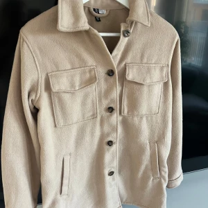 Beige jacka från H&M XS - Stilren beige overshirt/jacka perfekt till hösten från H&M i storlek XS. Mjuk kvalité. Jackan har två stora bröstfickor med lock, knäppning framtill med brunmelerade knappar och klassisk krage. Raka ärmar och enkel design.