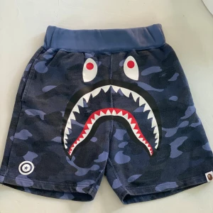 BAPE- A Bathing Ape Shorts  - BAPE – A Bathing Ape Shorts – Strl S – Streetwear-klassiker  Snygga shorts från A Bathing Ape (BAPE) – ett måste för dig som gillar streetwear. Använda endast ett fåtal gånger och i mycket fint skick. Typisk BAPE-stil med statement-look och kvalitet i varje detalj. 	•	Storlek: S 	•	Färg/mönster: [komplettera gärna med beskrivning, t.ex. camo, svart, logo etc.] 	•	Original – mycket fint skick 	•	Använda max ett par gånger