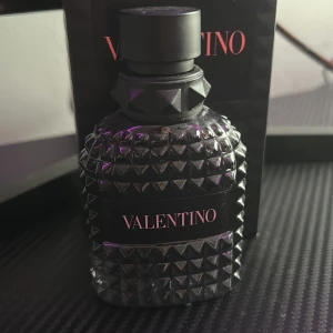 Valentino parfym i svart flaska - Elegant parfym från Valentino i en stilren svart flaska med nitar. Flaskan har en lyxig och modern design som passar perfekt på parfymhyllan. Doften är sofistikerad och tidlös, idealisk för den som vill ha något unikt och minnesvärt.