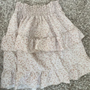 Blommig volangkjol - Kom privat för mer bilder om det söks, Söt kortkjol med blommigt mönster i ljusa färger. Kjolen har flera volanger och en elastisk midja för bekväm passform. Perfekt för varma dagar.