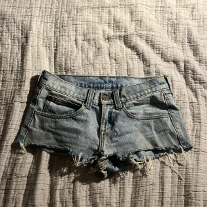 Blå jeansshorts med fransar - Säljer ett par blå jeansshorts med fransiga kanter. De har en klassisk femficksdesign och är perfekta för sommardagar. Dock har de ett hål på insidan i mitten.