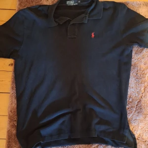 Svart pikétröja från Ralph Lauren - Snygg svart pikétröja från Ralph Lauren. Köpt här på plick men kom aldrig till användning. Lite för stor för mig. Den är M men passar även L. Perfekt nu till sommaren när man vill vara lite extra stilig. Den är i bra skick inga skador men kan se lite sliten ut. Skriv gärna om du har funderingar!