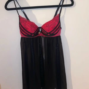 Playboy babydoll - Jättegullig babydoll från Playboy med push up som tyvärr inte passar mig längre. Bh-n är i en mörkare rosa med svarta blommiga spetsdetaljer. Den är även detaljerad med svarta band och en rosett i mitten med Playboy märket. Den har en öppen rygg.