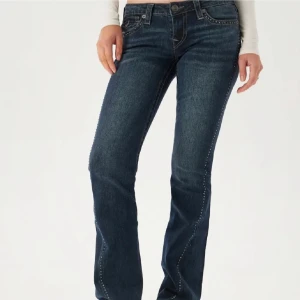 Mörkblå jeans med broderade detaljer - Snygga mörkblå jeans från True Religion med broderade detaljer på bakfickorna och nitar längs fickorna. De har en bootcut-stil och är lågmidjade, vilket ger en avslappnad och trendig look. Köptes i 31 march 2025 priset kan diskuteras🫶🏽