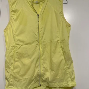 Gul väst från H&M - Säljer en ljusgul väst från H&M med dragkedja framtill. Västen har en enkel och stilren design, perfekt för lager-på-lager under vår och sommar.