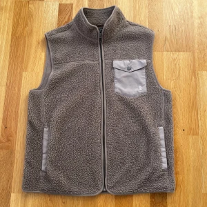 Beige fleeceväst från Bondelid - Säljer en mysig grå fleeceväst från Bondelid. Västen har en praktisk dragkedja framtill och en bröstficka med knapp. Perfekt för kyliga dagar.