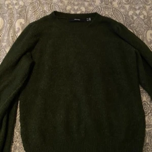 Mörkgrön stickad tröja från Vero Moda - Säljer en mysig mörkgrön stickad tröja från Vero Moda. Perfekt för kyliga dagar med sin klassiska design och långa ärmar. Tröjan har en rund halsringning och ribbade kanter för extra komfort.