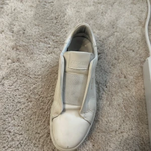 Vita sneakers från Axel Arigato - Snygga vita sneakers från Axel Arigato med en minimalistisk design. Skorna har en rund tå och är tillverkade i skinn med en tjock sula. Perfekta för en stilren look.