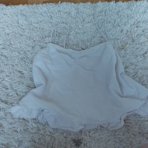 Vit randig linnetopp - Säljer en söt vit randig linnetopp med smala axelband och spetsdetaljer vid halsringningen. Perfekt för varma sommardagar. Toppen har en luftig passform och en lätt volang vid nederkanten. Kommer inte till användning längre så säljer den.