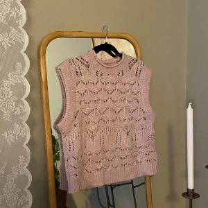 Rosa stickad väst - Säljer en söt rosa stickad väst med ett fint hålmönster. Västen har en ribbad kant vid ärmhålen och halsen, vilket ger en extra touch av stil. Perfekt för lager-på-lager under svalare dagar.