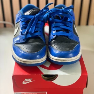 Nike Dunk Low ESS Game Royal /Black/ White  - Nike Dunk Low ESS WMNS “Game Royal / Black / White” Storlek: US 7 / EU 38 (24 cm) Snygga och stilrena Dunks i blått, svart och vitt. Använda men i bra skick – originalkartong ingår! Perfekta för dig som vill ha ett clean sneaker-par till våren.