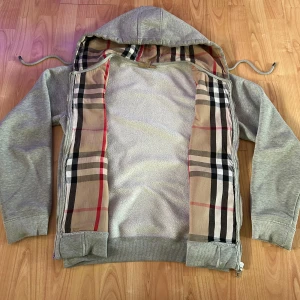 Burberry zip hoddie  - Grå burberry zip hoddie i st S. Den har det ikoniska rutiga burberry mönstret på insidan och grå utsida. Hör av er om frågor