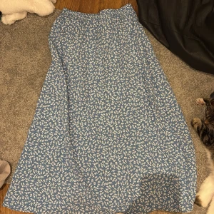 Blå blommig långkjol - Charmig blå långkjol med ett sött vitt blommönster. Kjolen har en avslappnad passform och är mycket bekväm. Har en slits på sidan. Är i storlek L. Aldrig använd då den är för stor för mig. 💙