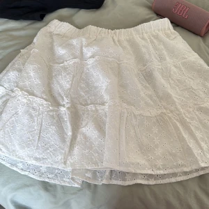 Vit kjol med broderad spets - Säljer en söt vit kjol från FB Sister med broderad spets och elastisk midja. Perfekt för varma dagar med sin luftiga design och fina detaljer. Passar bra till en enkel topp eller blus.