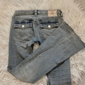 Ljusblåa jeans från True Religion - Snygga ljusblåa jeans från True Religion med  knappar i silver. Byxorna har en bootcut-stil och är lågmidjade. Midjemått 40 cm och innerben 85 cm. Har ändas andvänds en gång då jag köpte fel storlek, pris kan diskuteras💕💕