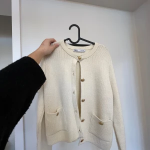 Beige stickad kofta från Zara - Säljer en beige stickad kofta från Zara med knappar i guld. I storlek L men sitter som en S.