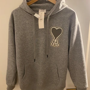 Grå hoodie från Ami - Säljer en stilren grå hoodie från Ami med ett hjärtmönster på bröstet. Tröjan har en klassisk passform med långa ärmar och en praktisk ficka framtill. Perfekt för en avslappnad look. Priset kan diskuteras.