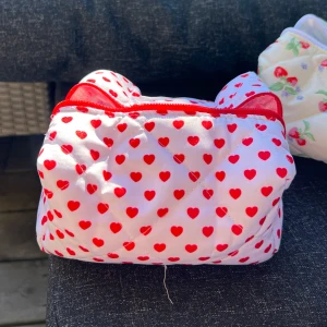Vit necessär med röda hjärtan - Söt vit necessär med röda hjärtan och dragkedja. Perfekt för att förvara smink eller småsaker. Den quiltade designen ger en mysig känsla och den röda insidan har ett rutigt mönster.