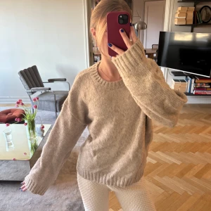 Beige stickad tröja - Säljer en mysig beige stickad tröja med rund hals och långa och breda ärmar. Perfekt för kyliga dagar och enkel att matcha med olika outfits. Tröjan har en avslappnad passform och ribbade kanter vid ärmslut och nederkant.