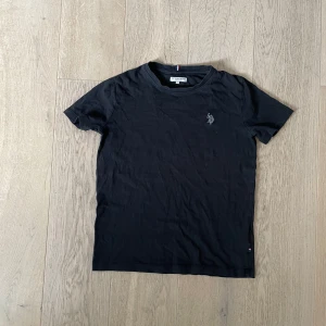 Svart t-shirt från U.S. Polo Assn. - Säljer en svart t-shirt från U.S. Polo Assn. med korta ärmar och en liten logga på bröstet. Perfekt för en avslappnad stil. T-shirten har en klassisk rund halsringning.
