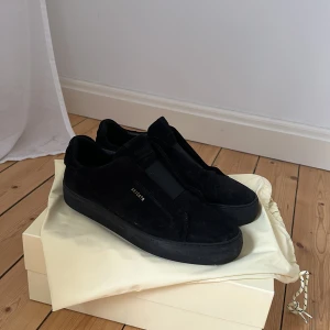 Svarta sneakers från Axel Arigato - Snygga svarta sneakers från Axel Arigato i mocka. De har en stilren design med rund tå och en diskret logga på sidan. Perfekta för en minimalistisk look.