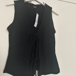 Svart ärmlös topp från Gina Tricot - Snygg svart ärmlös topp från Gina Tricot med knytning framtill. Toppen har en v-ringad design och är tillverkad i ett lätt material. Helt oanvänd med prislapp kvar. Ordinarie pris 259 kr. Storlek S!