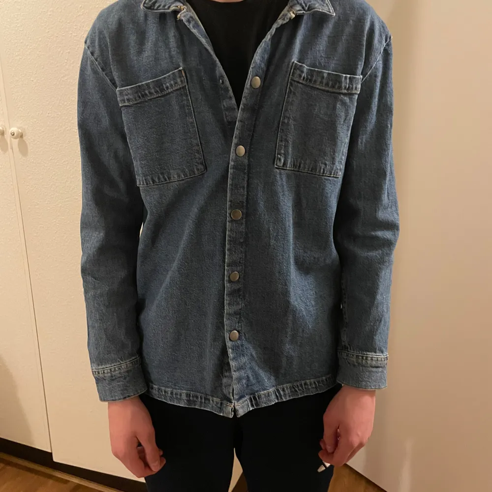 Säljer en snygg blå jeansskjorta från Lindex. Skjortan har långa ärmar och knappar framtill. Två bröstfickor ger en cool look. Perfekt för en avslappnad stil.. Paidat.