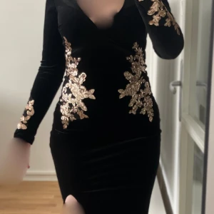 Svart sammetsklänning  med guldpaljetter - Elegant svart klänning med v-ringning och långa ärmar.  Storlek 34, kan även passa 36. Fler bilder kan skickas vid intresse. Hör av dig om du har frågor 