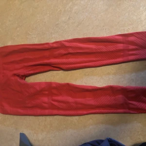 Röda träningstights från Casall - Snygga röda träningstights från Casall med hög midja och ribbad detalj vid midjan. Perfekta för gymmet eller yoga. Tightsen är tillverkade i ett stretchigt material som ger bra rörelsefrihet.