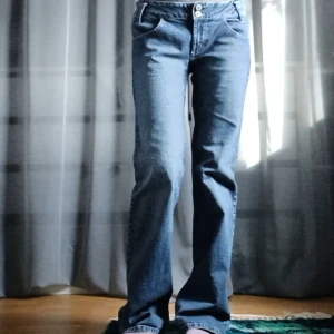 Blå bootcutjeans - Snygga blå jeans med utsvängd passform och låg midja. De har en klassisk femficksdesign och stängs med dragkedja och två knappar. Fint skick förutom lite slitna längst ned. Midjemått 39 cm, innerbenslängd 80 cm.