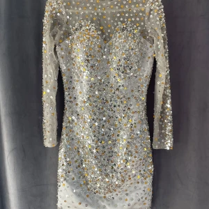Glittrig kortklänning med paljetter - Säljer en fantastisk glittrig kortklänning med paljetter i silver och guld. Klänningen har långärmade transparenta ärmar och en tight passform. Perfekt för en festlig kväll!