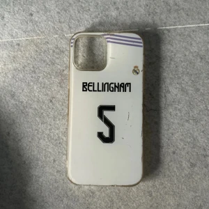 iPhone 12 mobilskal med Bellingham-tryck - Säljer ett vitt mobilskal med Bellingham-tryck och nummer 5. Skalet har en transparent kant och är designat för att passa en smartphone med en stor kameraöppning. Perfekt för fotbollsfans som vill visa sitt stöd.