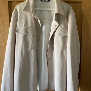 Zara overshirt  - Snygg beige overshirt med tryckknappar och två bröstfickor. Perfekt för lager-på-lager-stil. Den har en klassisk krage och långa ärmar.