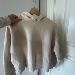 Beige hoodie - Säljer en stilren beige hoodie med en klassisk design. Den har en stor huva och ribbade muddar vid ärmslut och nederkant. Perfekt för en avslappnad look.