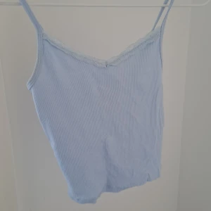 Ljusblått linne - Säljer en söt ljusblå ribbad linnetopp från H&M med spetsdetaljer vid halsringningen. Perfekt för varma dagar eller som ett lager under en tröja. Den har smala axelband och en mjuk, bekväm passform. I barnstorlek 134/146 men passar även 146-152💗🌺😘🎉
