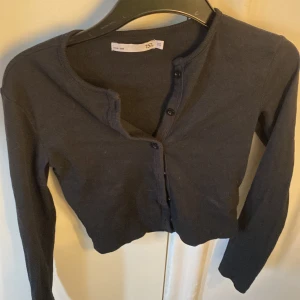 Svart kofta från 157 - Säljer en svart kofta från 157 i storlek XS. Koftan har långa ärmar och knappar framtill. Perfekt för lager-på-lager-stil och passar till många olika outfits.