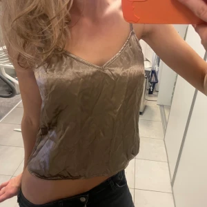 Beige satinlinne - Snyggt beige linne i satin med smala axelband och v-ringning. En knapp i ryggen saknas men kan lätt sys på. 