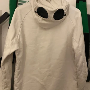 Vit hoodie med goggles från C.P. Company - Säljer en vit hoodie från C.P. Company med deras ikoniska goggles i huvan. Hoodien är autentisk och glasögonen tar man bara av när man ska tvätta och kör mjuktvätt