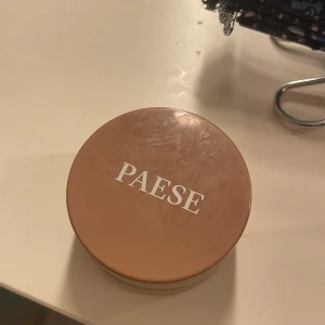PAESE bronzer i burk - Krämig bronzer från PAESE i en rund burk med skruvlock. Färgen är varm brun och ger en solkysst look. Perfekt för att framhäva ansiktskonturer och ge lyster till huden.