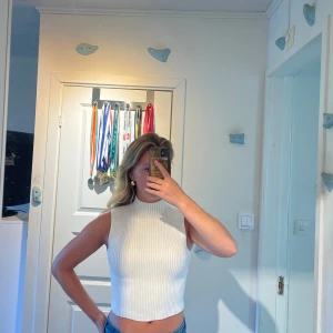 Vit stickad topp - Säljer en vit stickad top med hög hals. Toppen är ärmlös och har en tight passform. Storlek M men passar som S.