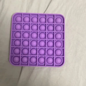 Lila pop it fidget-leksak - Säljer en fyrkantig pop it fidget-leksak i lila silikon. Perfekt för att stressa ner eller bara ha något att pilla med. Den har bubblor som kan tryckas in och ut på båda sidor.