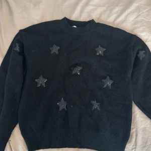 Svart stickad tröja med stjärnor från Gina Tricot - Säljer en svart stickad tröja från Gina Tricot med dekorativa svarta stjärnor framtill. Tröjan har rund halsringning och långa ärmar. Perfekt för dig som gillar en enkel men ändå unik stil!
