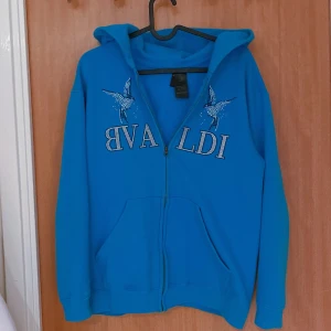 Bvaldi hoodie i Ljusblå  - Snygg blå hoodie med dragkedja och ett coolt tryck av fåglar och text på framsidan. Perfekt för en avslappnad stil med långa ärmar och en praktisk huva. Om man önskar så kan man såklart få flera bilder.