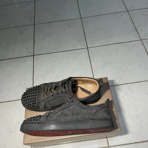 Christian Louboutins - Säljer ett par gråa sneakers från Christian Louboutin med mattsvarta nitar på tån och klassisk röd sula. Skorna har snörning och är tillverkade i mocka med gråa detaljer. Perfekta för dig som vill sticka ut med en lyxig touch. Pris går att diskuteras. Säljs pga att de ej passar mig allt e bra förutom att lite smuts satt sig på undersidan men har man rätt bortttagningdmedel borde man få bort de mesta, en ring saknas även från skorna vid sidan annars är de riktigt goa skor👌💪💯