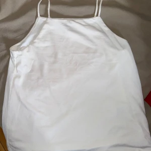 Vit linnetopp med smala axelband - Säljer en enkel och stilren vit linnetopp med smala axelband och rak halsringning. Perfekt att matcha med jeans eller kjol för en clean look. Tunt och lätt material som passar bra till varma dagar.